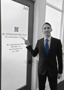 Attorney standing in front of office door and pointing at law firm's name and logo.